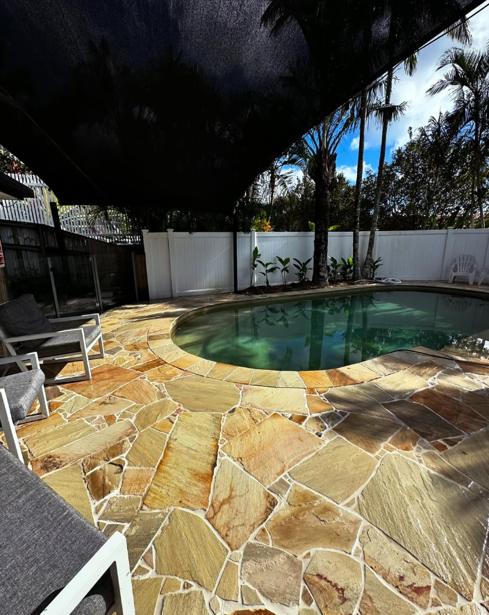 Sandstone crazy paving pool surround under a shade sail