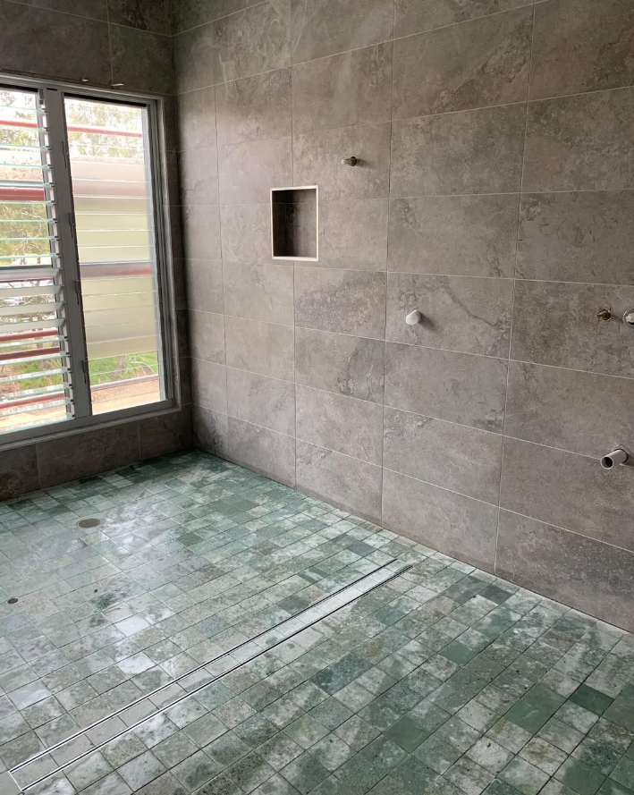 Bathroom with large format stone-look wall tiles, shower niche and green mosaic floor