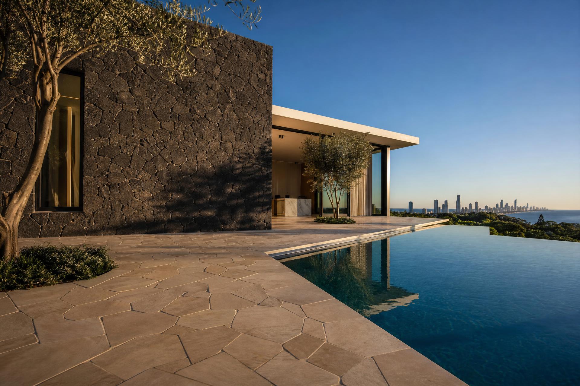 Basalt stone cladding wall and travertine crazy paving beside an infinity pool